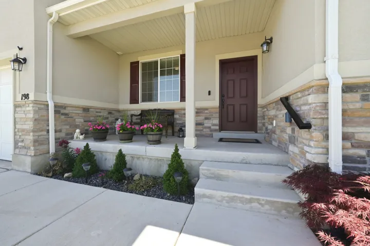 Covered entry porch featuring a paneled door, stone veneer detailing, and a concrete approach