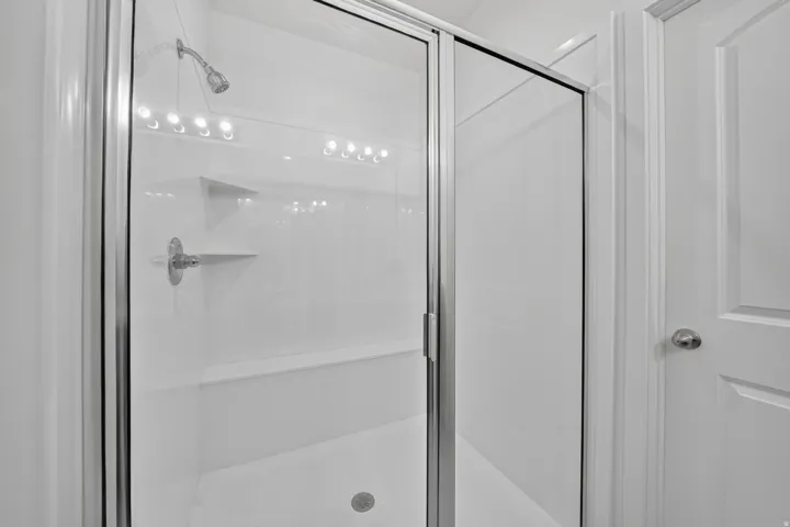 White shower enclosure featuring a glass sliding door, integrated shelving, and a built-in bench