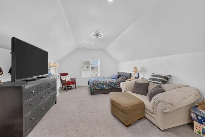 Spacious room featuring vaulted ceilings, light gray carpet flooring, a window offering natural light, white painted walls, and a modern ceiling light fixture