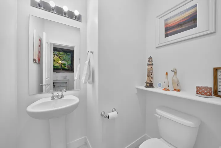 White pedestal sink with a chrome faucet, illuminated by a four-bulb vanity light fixture