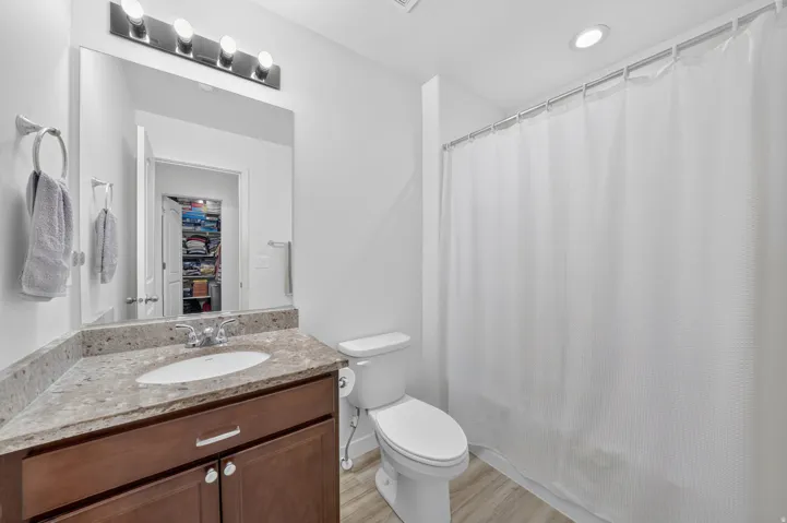 Full bathroom featuring a wood-finish vanity with a stone countertop, an undermount sink, and a modern light fixture