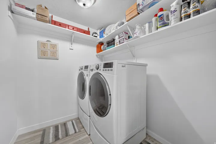 Dedicated laundry area featuring a front-load washer and dryer, wood-finish flooring, and wall-mounted shelving for organized storage