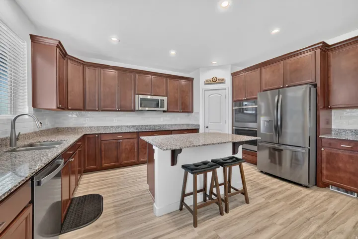 Kitchen featuring wood-finish cabinetry, speckled countertops, stainless steel appliances, a center island with built-in support, and light wood-look flooring