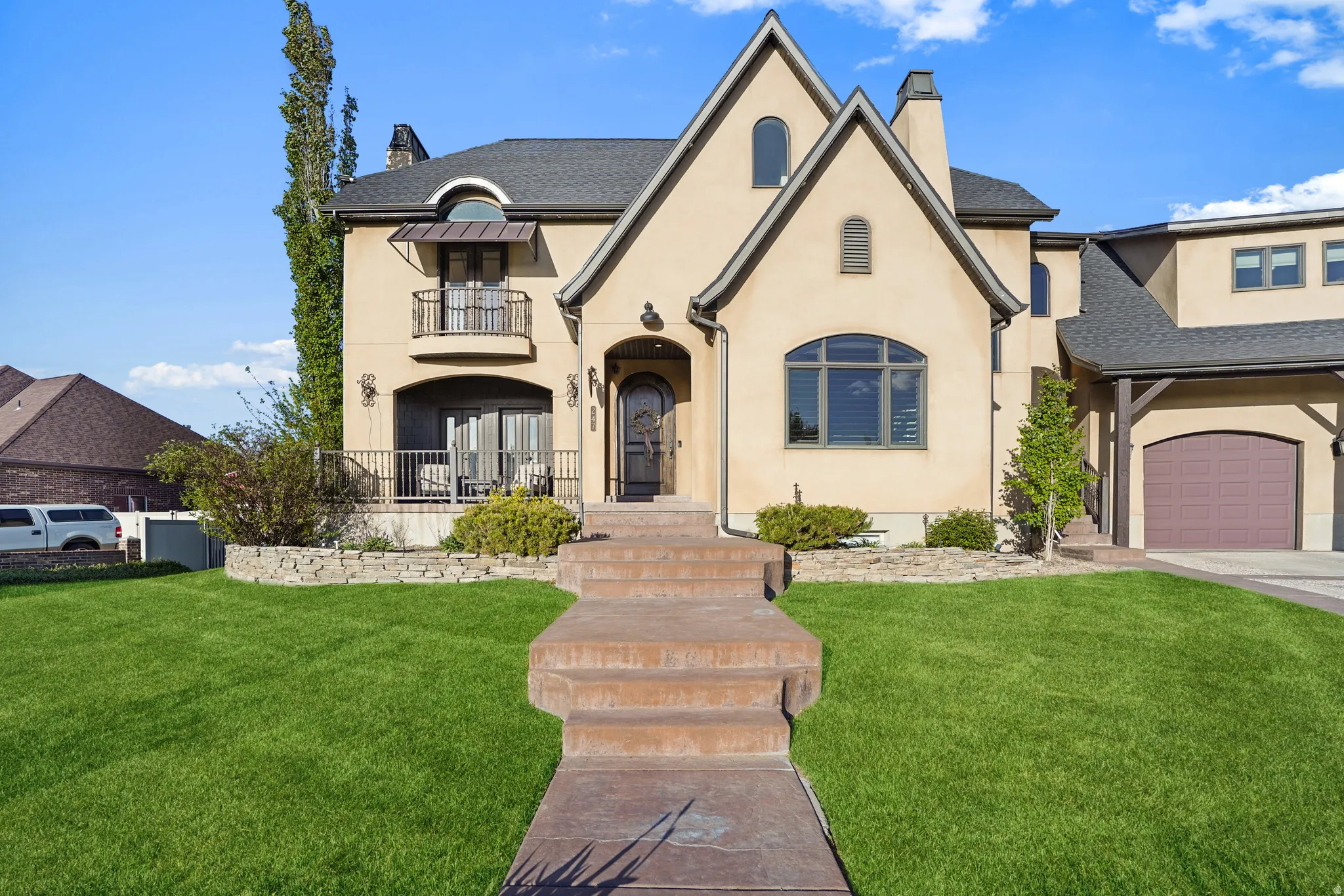 French provincial home featuring a chimney, stucco siding, a front lawn, and a balcony