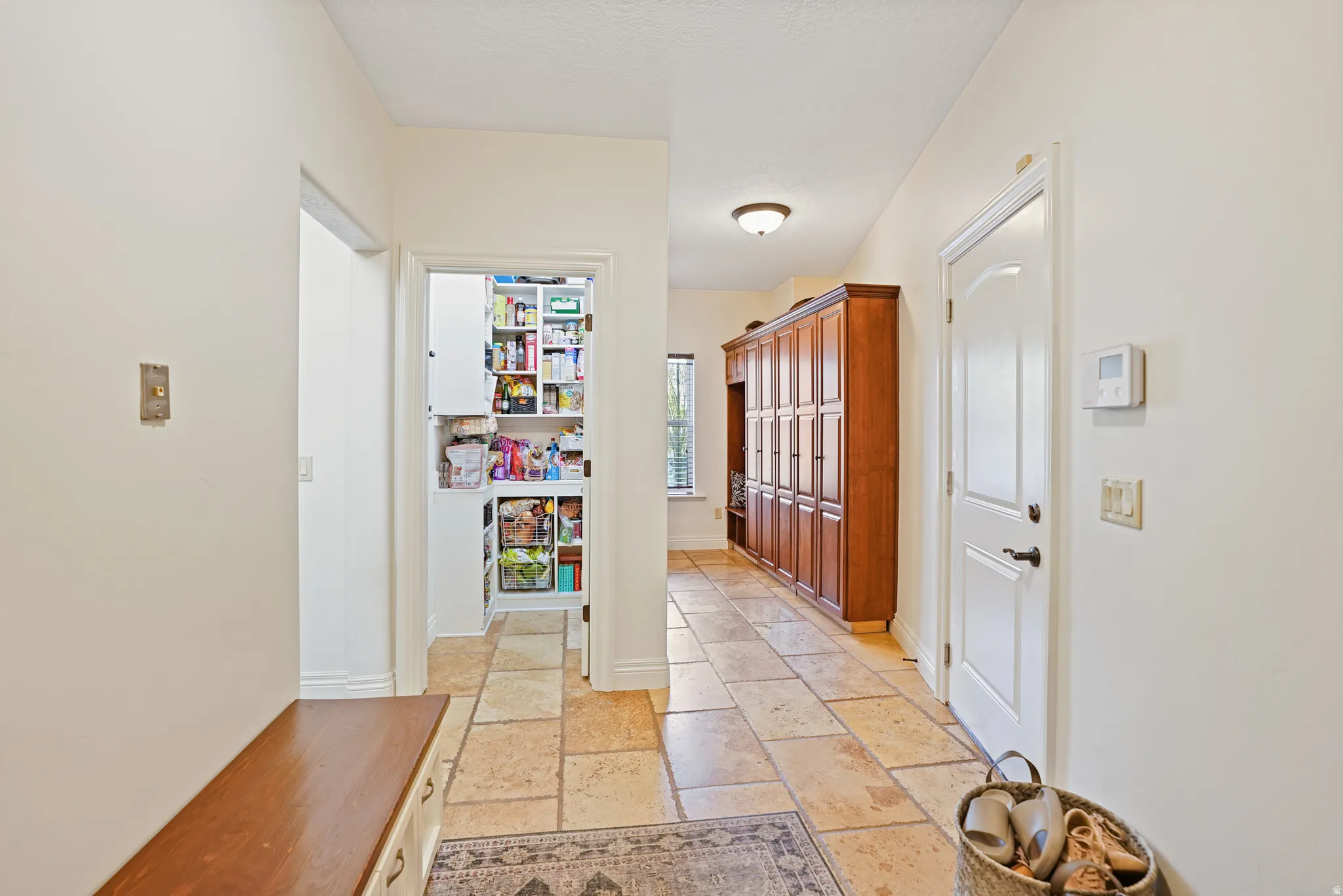 Hallway featuring stone tile floors and baseboards. Mudroom and pantry.