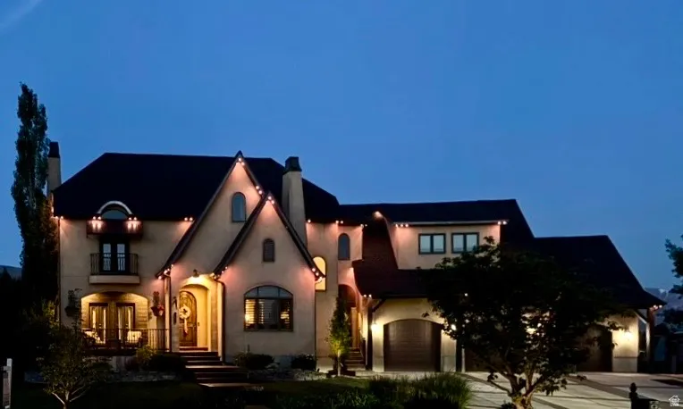 Stately exterior featuring a prominent gabled entry, arched windows, a multi-car garage, and a second-story balcony with iron railings