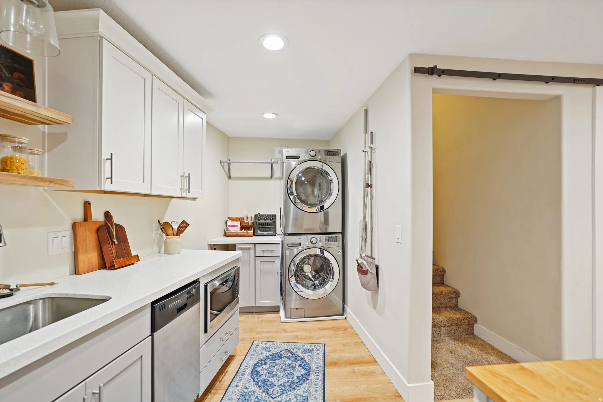 basement aundry area featuring light wood-type flooring, recessed lighting, stacked washing machine and dryer, and a barn door