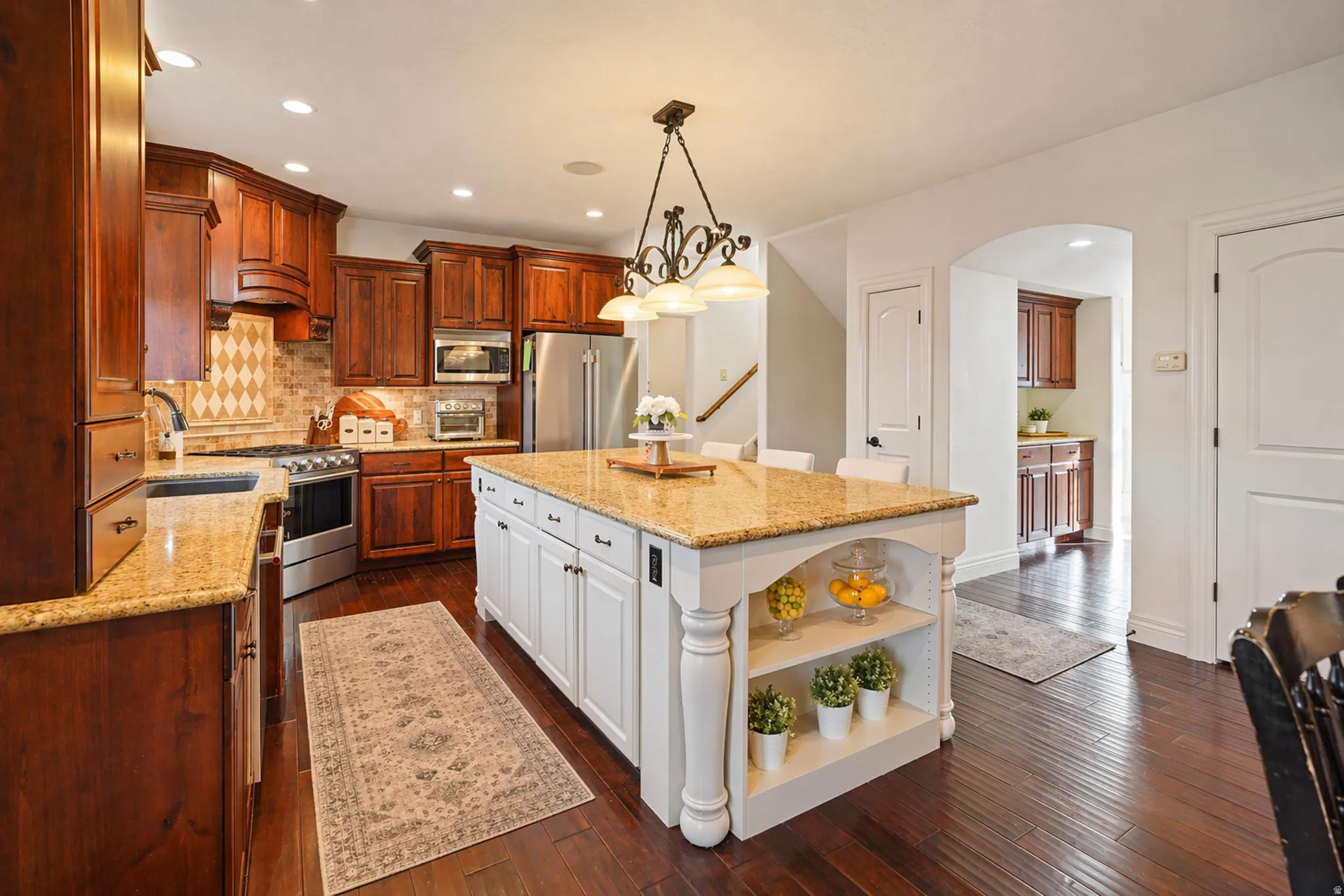 Kitchen with open shelves, dual tone cabinets, light stone counters, dark wood-style floors, and premium appliances