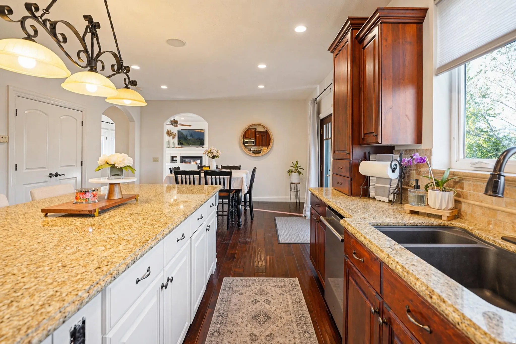 Kitchen with arched walkways, dark wood finished floors, light stone countertops, and decorative light fixtures