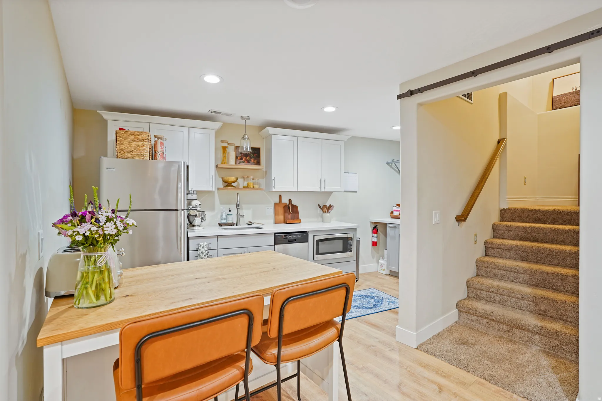 Basement kitchen featuring stainless steel appliances, light wood finished floors, a kitchen bar, white cabinets, and wood counters
