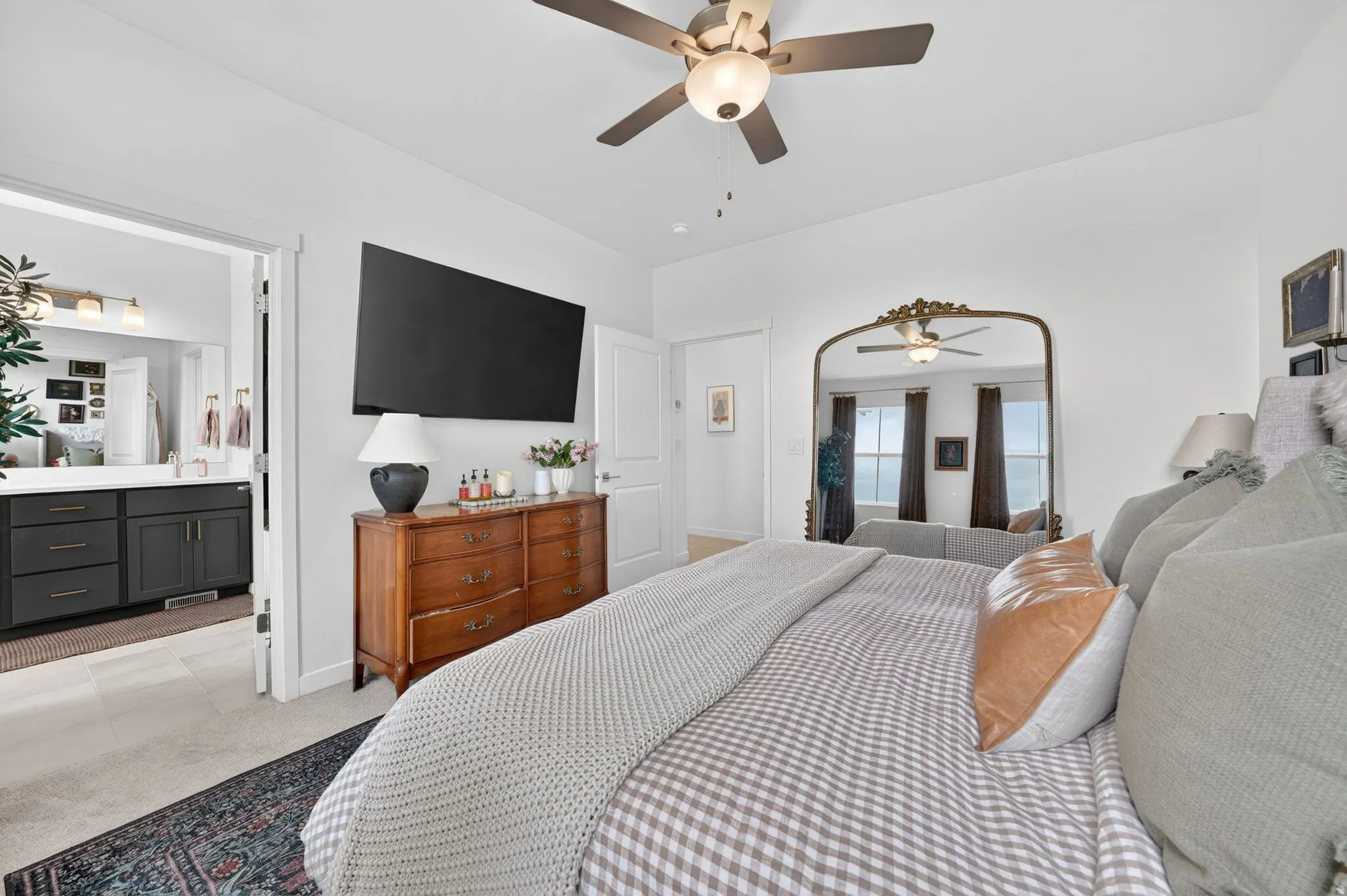 Bedroom featuring ceiling fan, light carpet, and ensuite bathroom