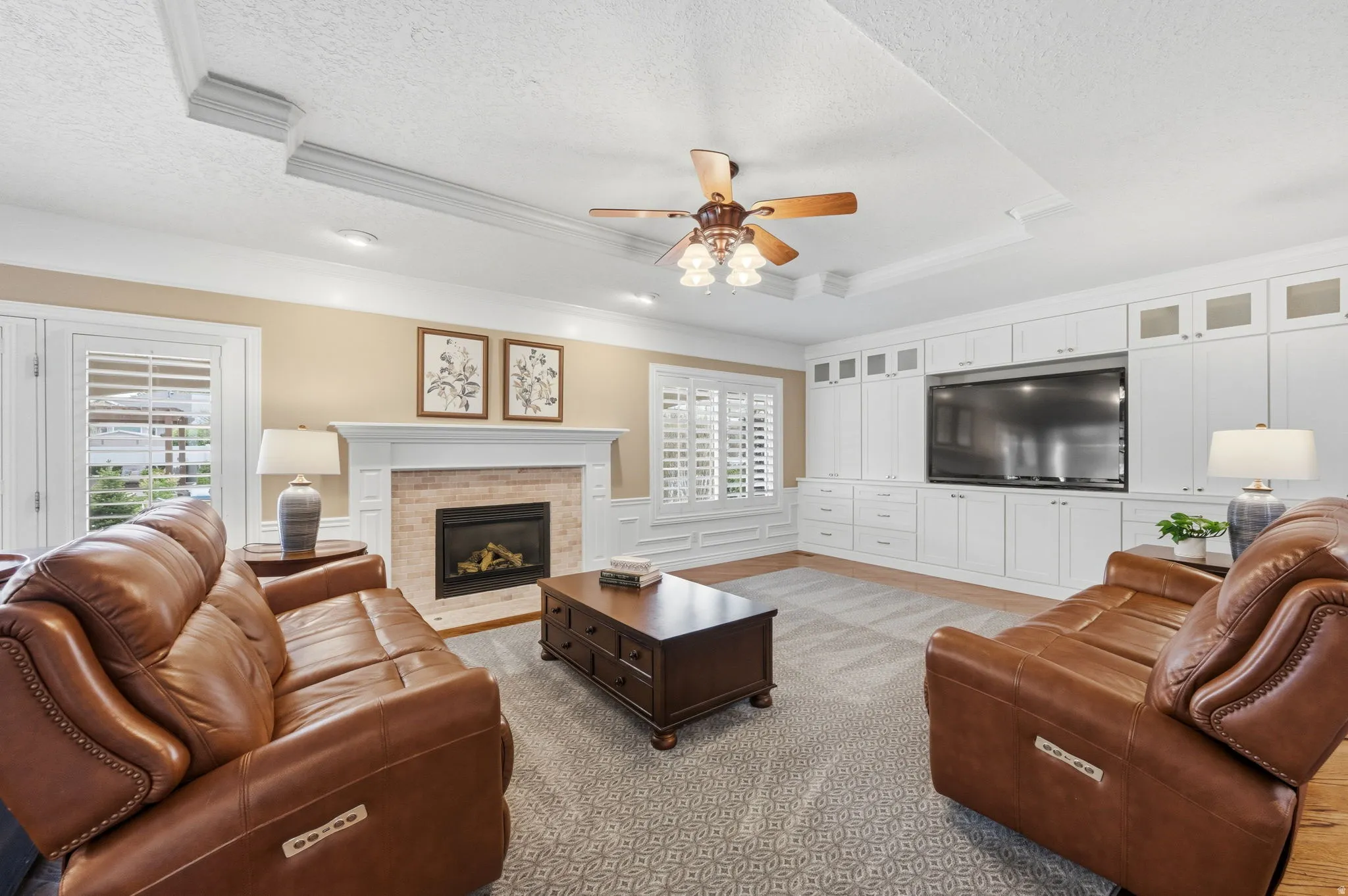 Living room with a ceiling fan, crown molding, wainscoting, a fireplace, coffer ceiling and custom built in entertainment center