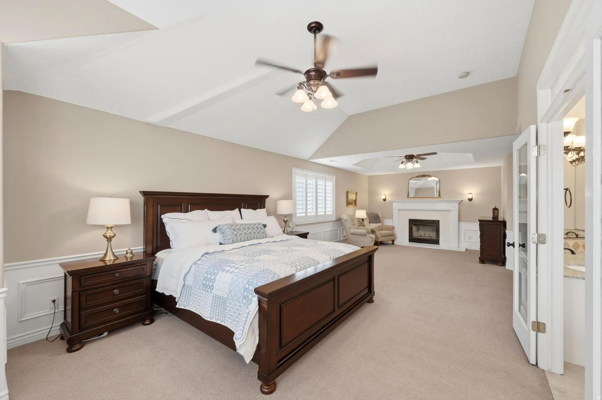 Primary bedroom with wainscoting, a decorative wall, fireplace, and vaulted ceiling