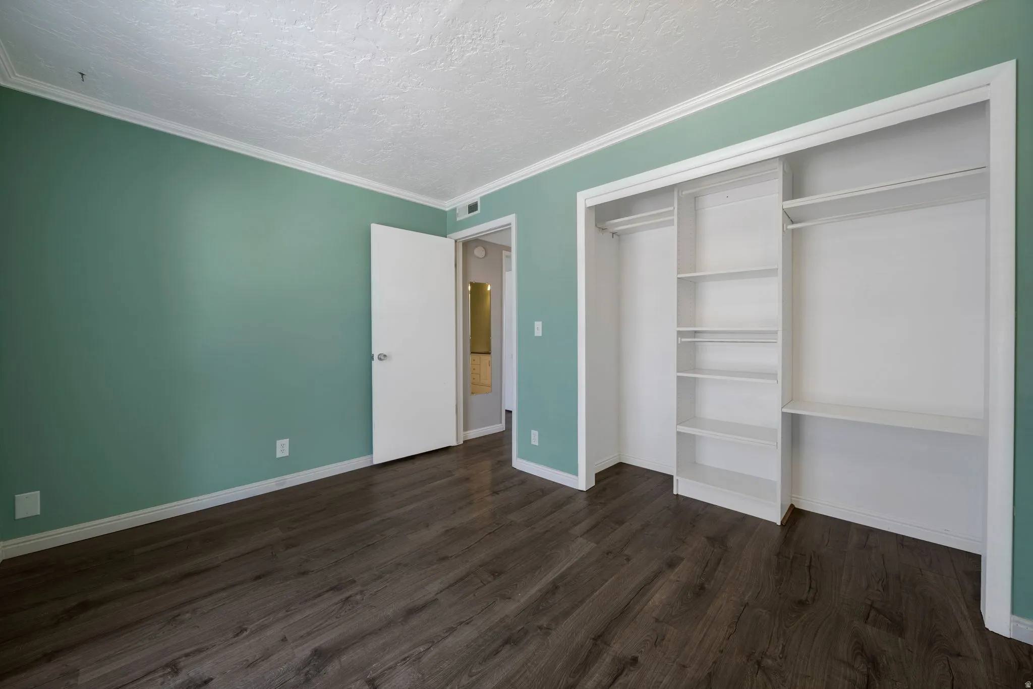 Unfurnished bedroom featuring a closet, dark wood-style floors, crown molding, and a textured ceiling