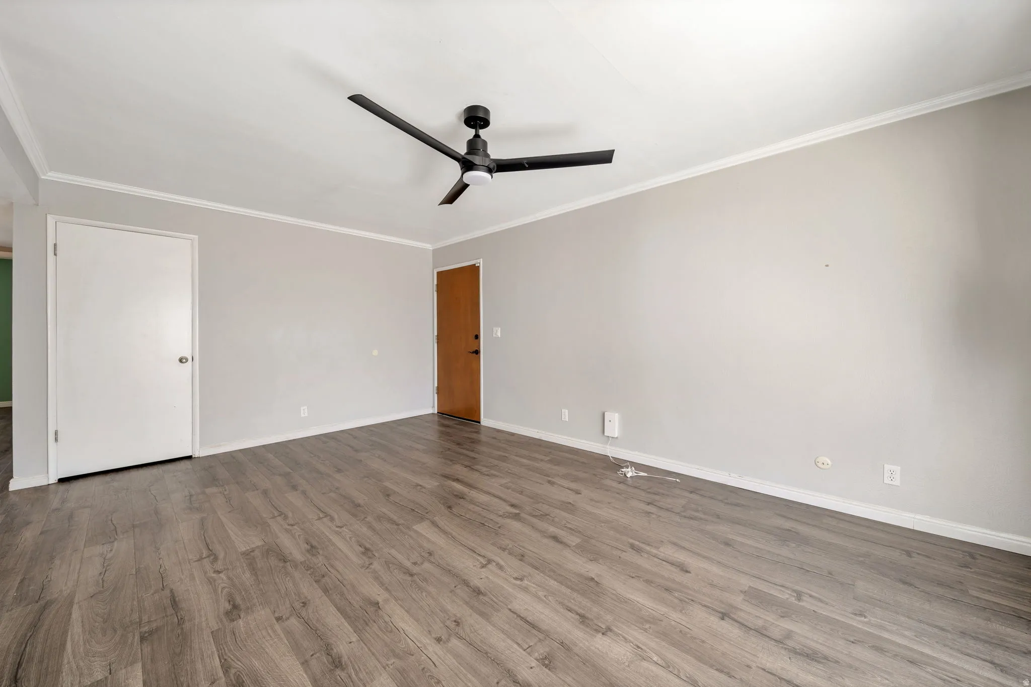 Empty room featuring dark wood-style floors, ornamental molding, and a ceiling fan