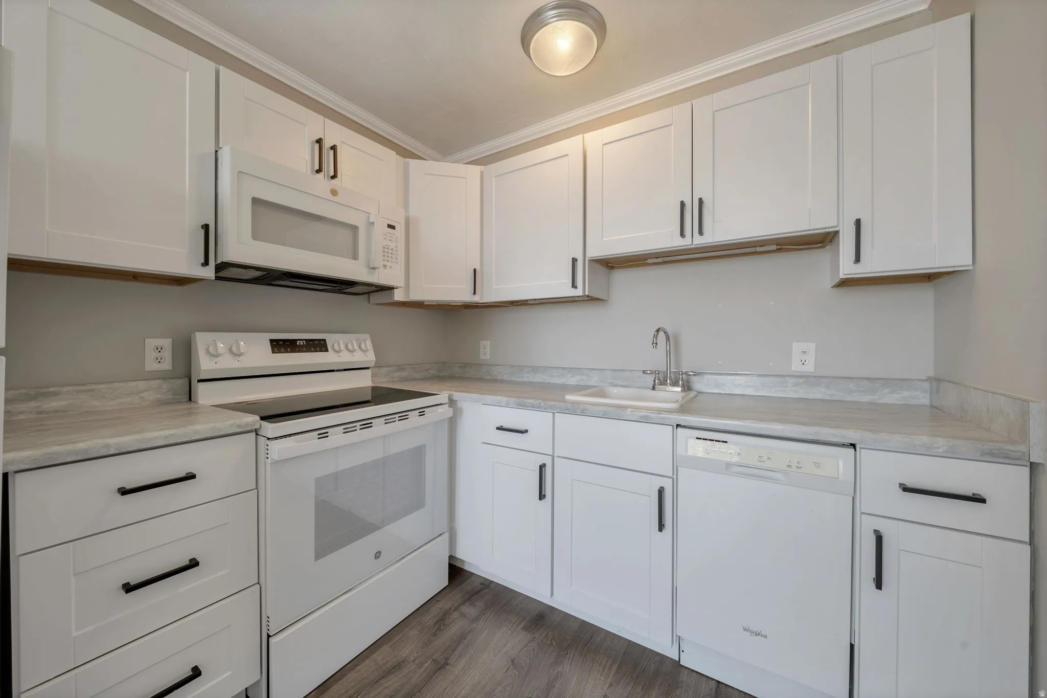 Kitchen featuring white appliances, light countertops, white cabinets, and crown molding