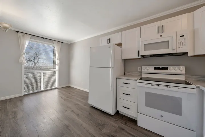 Kitchen with white appliances, white cabinetry, light countertops, ornamental molding, and dark wood-style floors