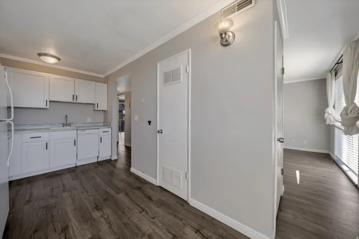 Kitchen with ornamental molding, light countertops, white cabinets, dark wood-type flooring, and dishwasher