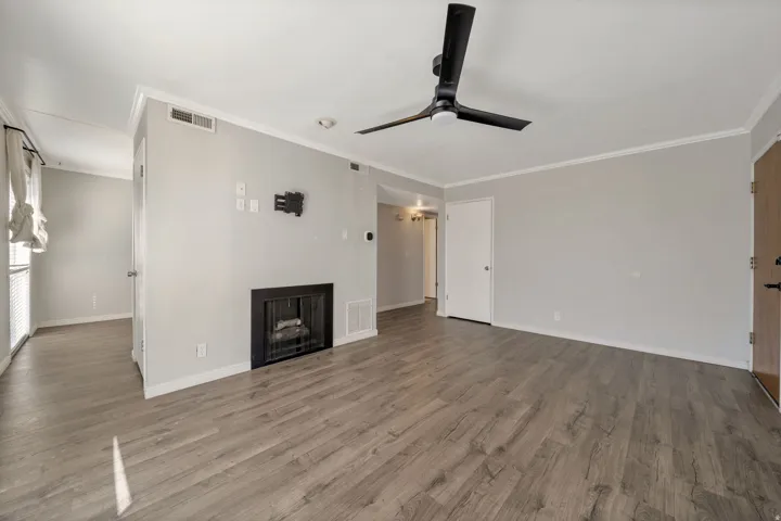 Unfurnished living room featuring crown molding, ceiling fan, a fireplace, and dark wood-type flooring