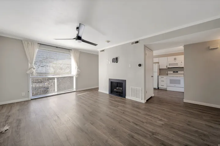 Unfurnished living room featuring a ceiling fan, crown molding, a fireplace, and dark wood-style flooring