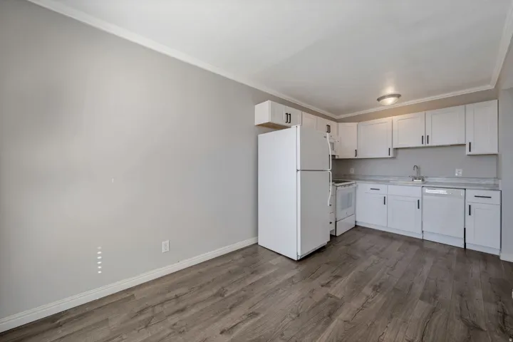 Kitchen featuring white appliances, light countertops, crown molding, white cabinetry, and dark wood-style flooring