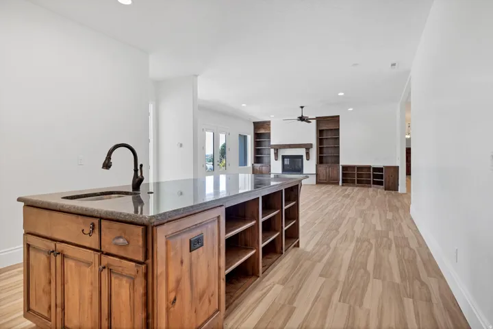 Kitchen with a glass covered fireplace, a center island with sink, recessed lighting, open shelves, and wood finish cabinets