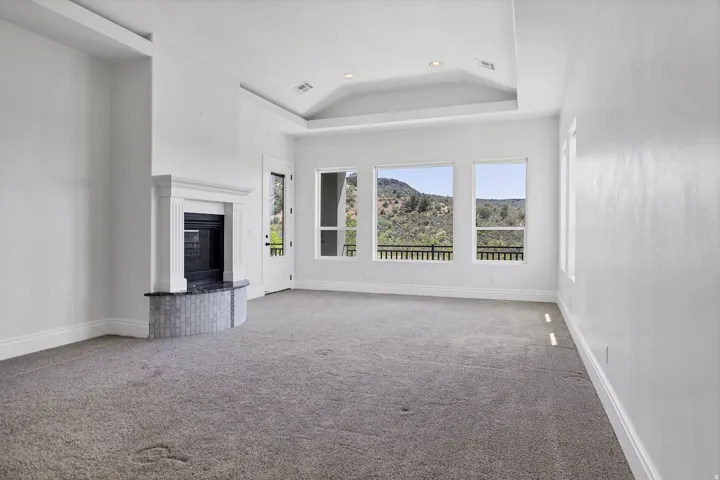 Unfurnished living room featuring carpet flooring, a glass covered fireplace, recessed lighting, lofted ceiling, and a raised ceiling