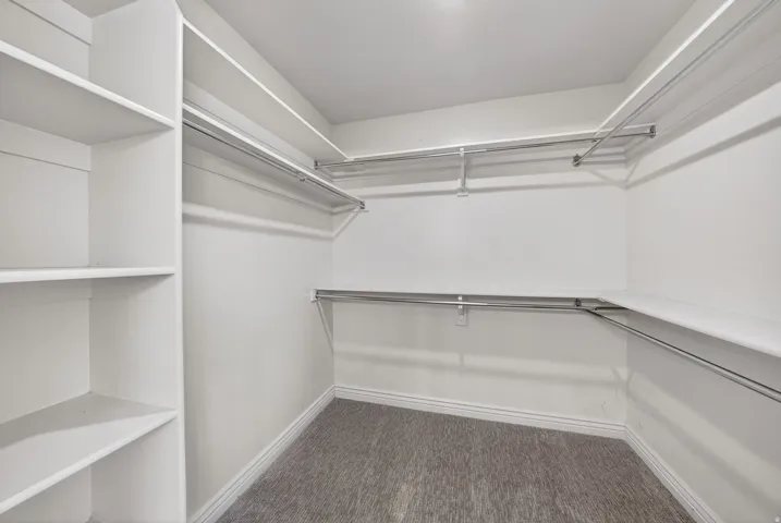 Walk-in closet featuring built-in shelving, multiple hanging rods, white walls, white baseboards, and grey patterned carpeting
