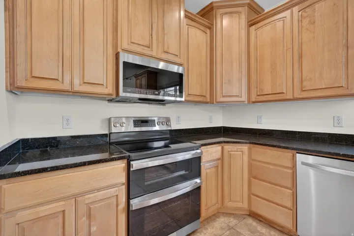 Kitchen featuring wood cabinetry, stainless steel appliances, dark countertops, and tile flooring