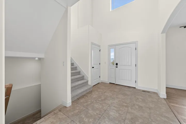 Two-story foyer with a vaulted ceiling, tile flooring, and a carpeted staircase