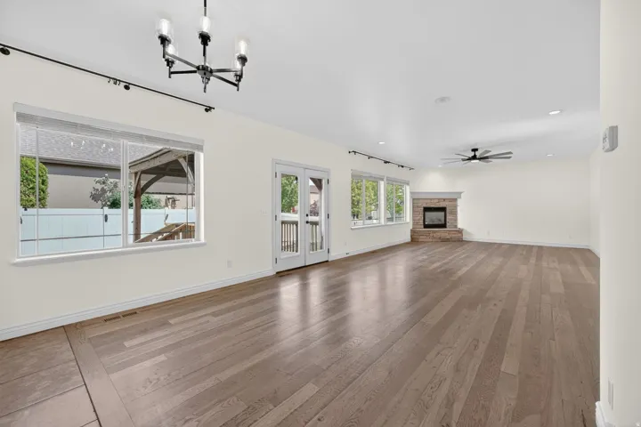 Spacious room featuring wide plank wood-finish flooring, a stone-surround fireplace, and multiple large windows