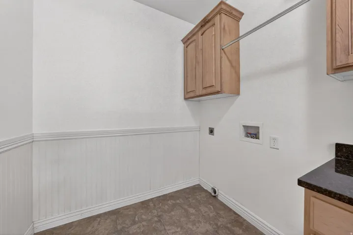 Laundry area featuring wood cabinetry, a hanging rod, wainscoting, and a granite-look countertop