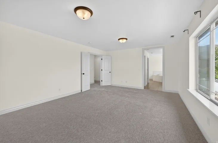 Spacious room featuring neutral carpeting, light-toned walls, and a large window providing natural light