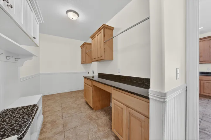 Utility room featuring built-in cabinetry, dark countertop, ceramic tile flooring, and white wainscoting
