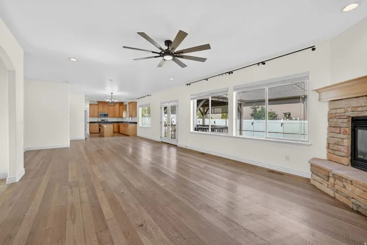 Expansive living space featuring wood-finish flooring, a stone-clad fireplace, and a contemporary ceiling fan