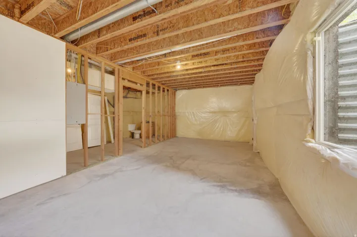 Unfinished basement featuring exposed wood joists, concrete flooring, and a framed wall structure