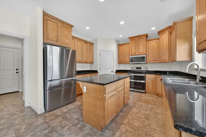 Kitchen featuring an island with a dark countertop, light wood cabinetry, stainless steel appliances, and tile flooring