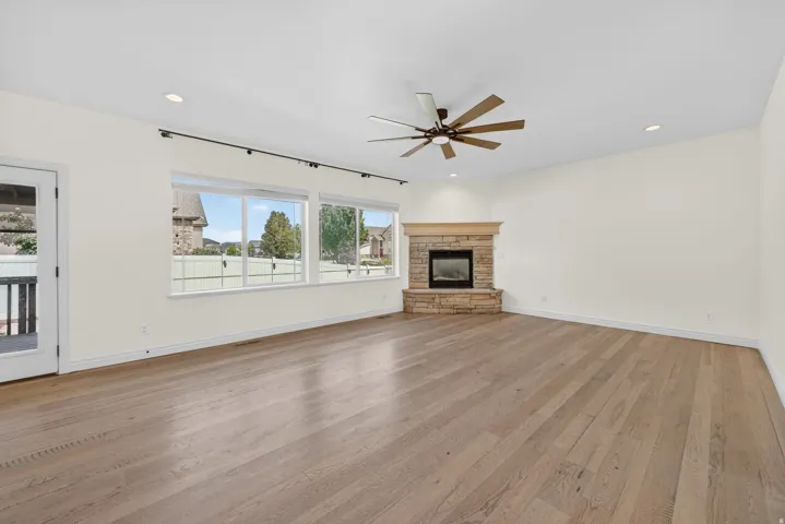 Spacious room featuring wood-finish flooring, a corner stone-faced fireplace with a wood mantel, and a multi-blade ceiling fan