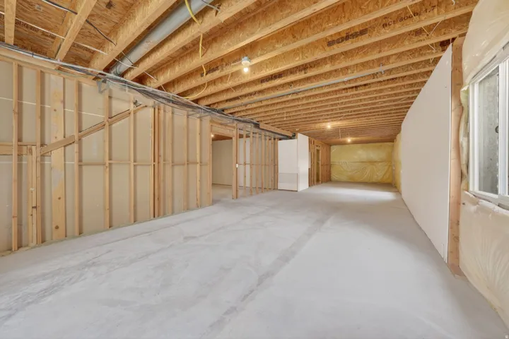 Expansive unfinished basement featuring a concrete floor, exposed wood ceiling joists, framed interior walls, partial drywall installation, and a window with insulation