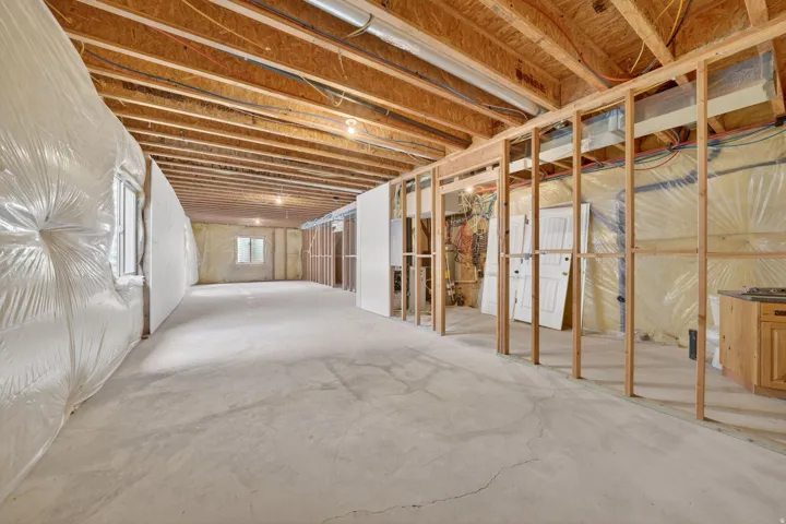 Unfinished basement with concrete flooring, exposed wood joists, framed interior walls, and visible insulation