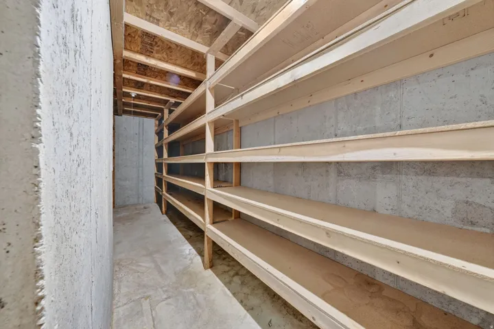 Spacious storage area featuring extensive built-in wooden shelving, exposed concrete walls, and a concrete floor