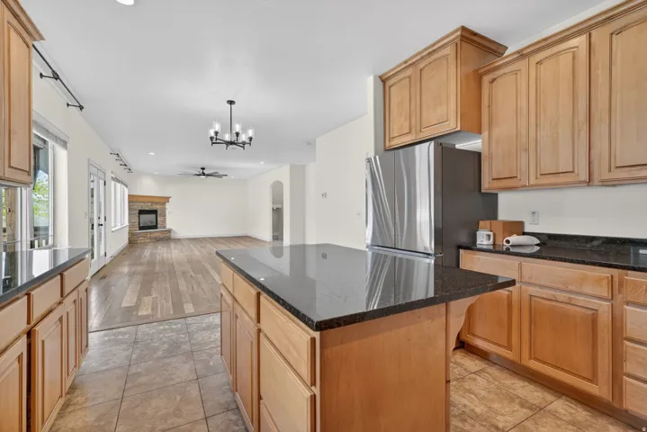 Open-concept kitchen featuring an island with a black countertop, natural wood-finish cabinetry, and stainless steel appliances