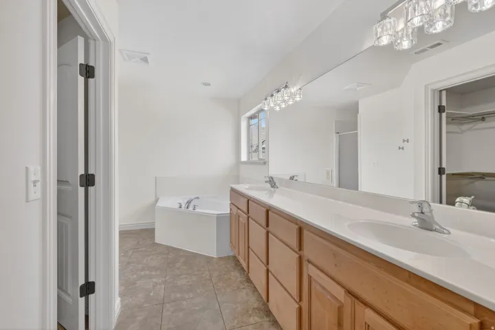 Bathroom featuring a dual vanity with wood cabinetry and white countertops, a large framed mirror, and a corner soaking tub