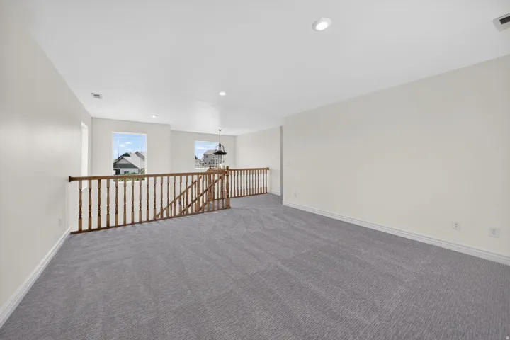 Open loft space featuring light gray carpeting, neutral wall finishes, recessed lighting, and a chandelier fixture