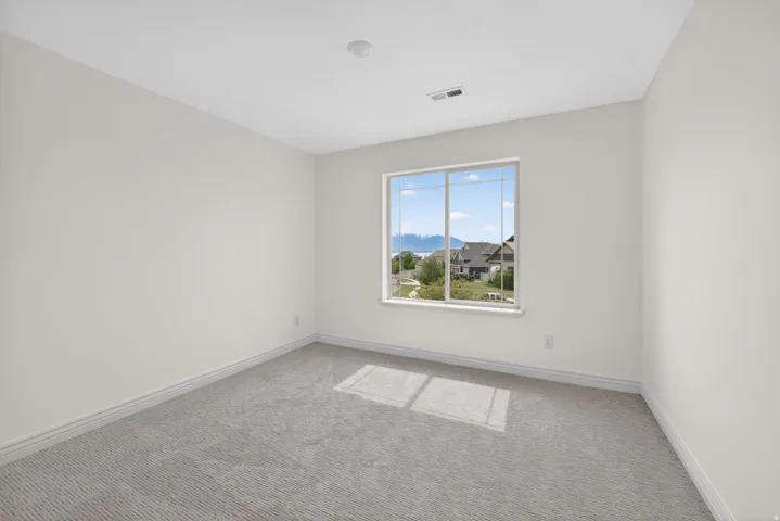 Bright room featuring neutral wall paint, gray patterned carpet, white trim, a recessed ceiling light, and a large window overlooking distant mountains and residential properties