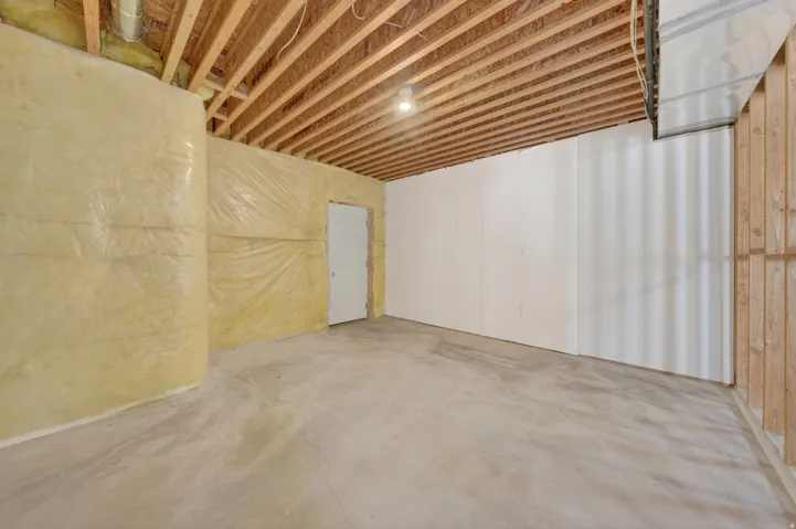 Unfinished basement featuring exposed wood ceiling joists, insulation-wrapped walls, and a concrete floor