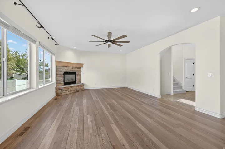 Spacious main living area featuring wide-plank wood-finish flooring, a stone-clad fireplace with a wood mantle, and an array of large windows