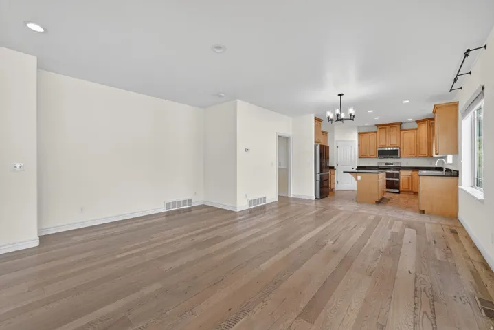 Open-concept living space featuring wood-finish flooring, recessed lighting, and a kitchen with warm-toned cabinetry, dark countertops, and stainless steel appliances