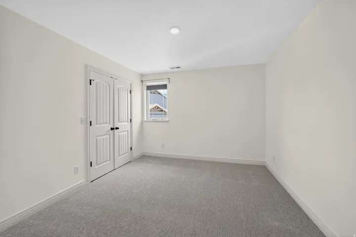 Carpeted room featuring light-colored walls, a single window with blinds, and white bi-fold doors with black hardware