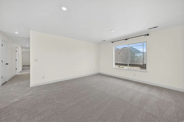 Spacious room featuring neutral carpeting, recessed lighting, and a large window providing natural light